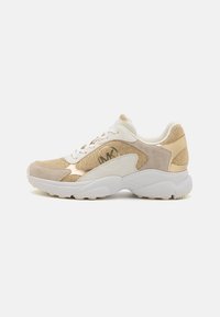 Sneakers i beige og gull med en teksturert stoffoverdel, suedeceller og hvit gummisål. Har lisser og en logo detalj på siden.