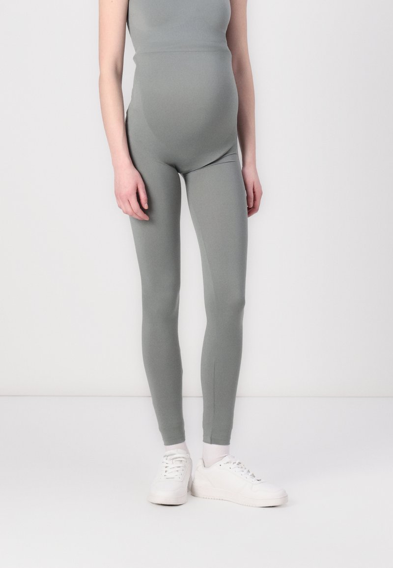 Leggings de maternidade em um tecido verde suave e apagado. Design ajustado com uma textura lisa e sem padrões visíveis. Combinados com tênis brancos.