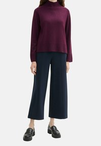 Un pull à col montant bordeaux, en texture tricotée, associé à un pantalon large bleu marine et des mocassins noirs à plateforme, créant un look superposé.