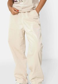 Beige wijde broek gemaakt van glad, glanzend stof met zijzakken en subtiele branding op de heup.