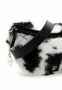 Borsa in finta pelliccia a stampa muccata bianca e nera con tracolla in pelle nera, chiusura con zip e etichetta logo in argento. Texture morbida con un aspetto lanoso.