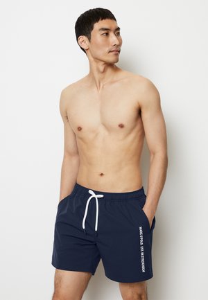 Shorts de bain navy avec cordon blanc, poches latérales et logo imprimé le long de la jambe gauche. Tissu lisse et léger, design de longueur genoux.