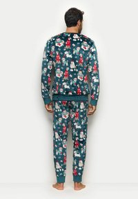 Bawełniany komplet piżamowy z długimi rękawami i spodniami. Posiada turkusowe tło z figlarnym psem i świątecznym wzorem w czerwonym i białym kolorze.