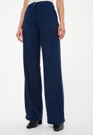 Marineblaue, weit geschnittene Hose mit weißen Nadelstreifen, hoher Taille, vorderer Knopfleiste, kombiniert mit schwarzen spitzen Stiefeletten.