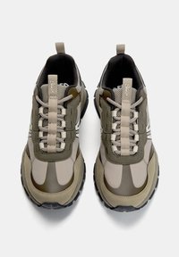 Sportliche Sneakers mit einem Obermaterial aus Netz und Synthetik in Olivgrün und Beige, mit einer strukturierten Sohle und kontrastierenden Schnürsenkeln.