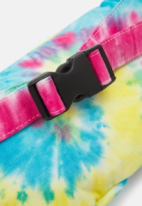 Czarna plastikowa klamra na różowym pasku przymocowanym do materiału w niebiesko-żółto-zielony wzór tie-dye.