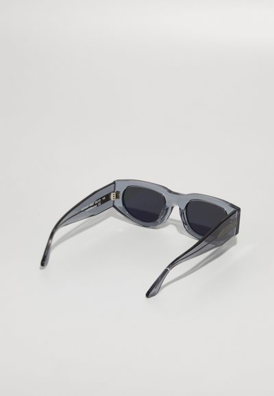 Lunettes de soleil grises avec une monture transparente, des verres foncés et des branches fines présentant un motif texturé sur les côtés.