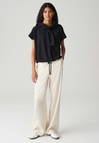 Zwart geblokt shirt met korte mouwen en een halsband, gecombineerd met losse witte broeken en witte sneakers, wat een ontspannen pasvorm laat zien.