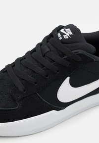 Nike SB sneakers featuring a black suede and textile upper, white logo accents, and flat black laces, with a textured rubber sole.