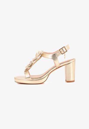 Sandalo metallizzato dorato con tacco, design a cinturino a T, con dettagli floreali sovrapposti, tacco largo e fibbia di chiusura.