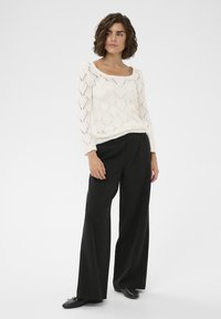 Fehér kötött pulóver gyémántmintával, négyzet alakú dekoltázs, hosszú ujjak, laza fekete nadrággal és fekete cipővel párosítva.