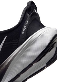 Ασπρόμαυρο αθλητικό παπούτσι Nike με ετικέτα "easyon" και πλεκτό επάνω μέρος, γωνιακά τοποθετημένο ώστε να φαίνεται η υφή της σόλας και το λουράκι στη φτέρνα.