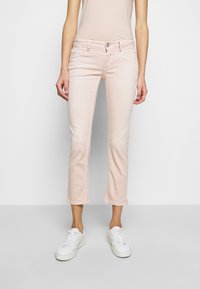 Jean court rose pâle en tissu mélangé de coton extensible. Comprend des poches avant, une braguette zippée et une fermeture à bouton. Porté avec des baskets blanches.