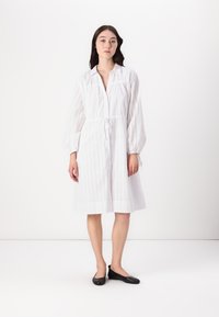Rochie albă, până la genunchi, cu mâneci lungi tip balon, deschidere cu nasturi și talie cu șnur. Prezintă un design cu perforații pentru textură și circulație a aerului.