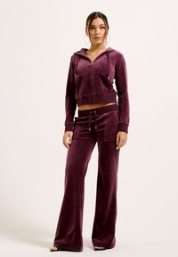 Completo di velluto viola composto da un hoodie corto con zip e tasche frontali e pantaloni con vestibilità comoda e tasche laterali.