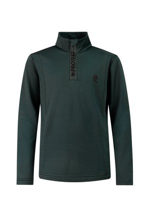 Jonge jongen staat, draagt een donkergroene lange mouwen met rits top, lichtgrijze broek en zwarte schoenen, tegen een effen lichte achtergrond.