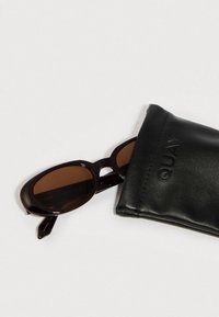 Barna ovális napszemüveg fényes keretben, fekete bőr tokban, dombornyomott márkajelzéssel. A lencsék barnára színezettek.