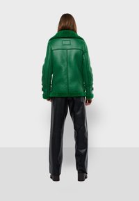 Zelená shetl-točená bunda s chuchvalcovým golierom, bočnými prackami, prešitými detailami a priamym strihom, v kombinácii s čiernymi koženými nohavicami.