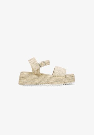 Sandales compensées beiges tissées avec deux sangles ajustables et une boucle. Semelle en jute texturée avec une semelle extérieure en caoutchouc blanc.