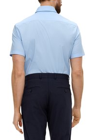 Hellblaues Kurzarmhemd mit einem ordentlichen Kragen, glatter Textur, kombiniert mit dunkelblauen Hosen, die zwei Gesäßtaschen und eine Knopfdetaillierung aufweisen.