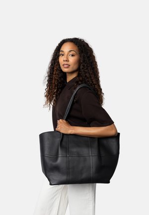 Borsa tote nera in pelle con una forma strutturata, caratterizzata da cuciture orizzontali e una texture liscia. Tenuta da un modello su uno sfondo neutro.