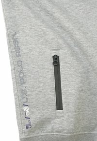 Felpa grigia con una texture liscia, dotata di una tasca con zip e un branding ricamato di colore blu scuro sul lato.