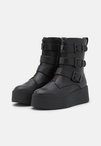 Bottines noires en similicuir, dotées de trois lanières réglables avec boucles, d'une fermeture éclair latérale et d'une semelle épaisse à plateforme.