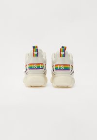Sneaker bianchi con suola spessa. Il retro a strisce arcobaleno presenta il testo "LOVE IS LOVE". Texture liscia con dettagli colorati.