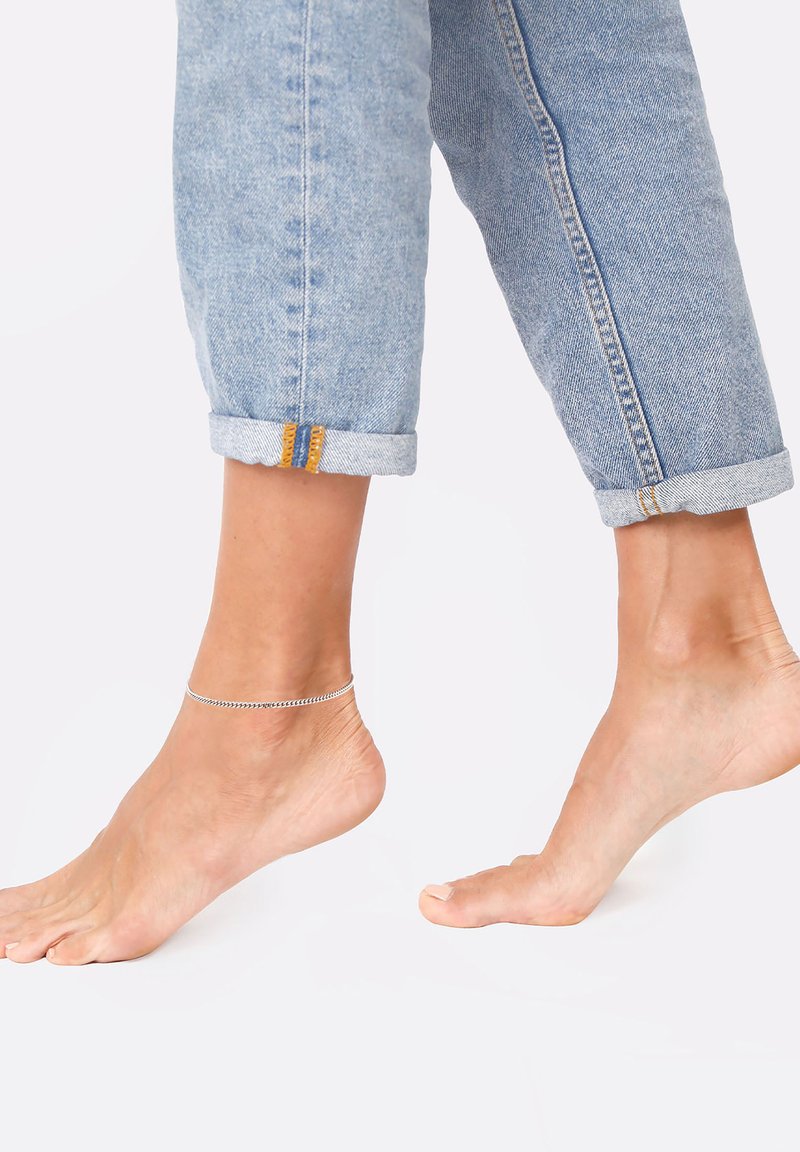 Lysblå denim jeans med oprullede kanter, prydet med orange syninger, parret med en bar fod iført et sølvanklet.