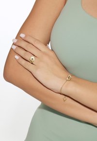 Gold ring with a twisted design and a clear accent stone, paired with a delicate gold bracelet featuring a small triangular charm.