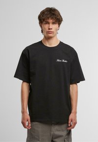Black cotton t-shirt with oversized fit, ribbed crew neckline, short sleeves, and white "Hani Studios" text embroidered on the chest.