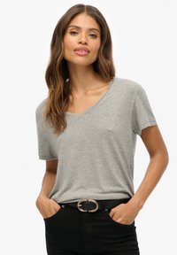 Grau kurzärmliges V-Ausschnitt-T-Shirt aus weichem Material, kombiniert mit einem schwarzen Gürtel mit einer goldenen Doppelschlaufen-Schnalle, getragen mit schwarzen Hosen.