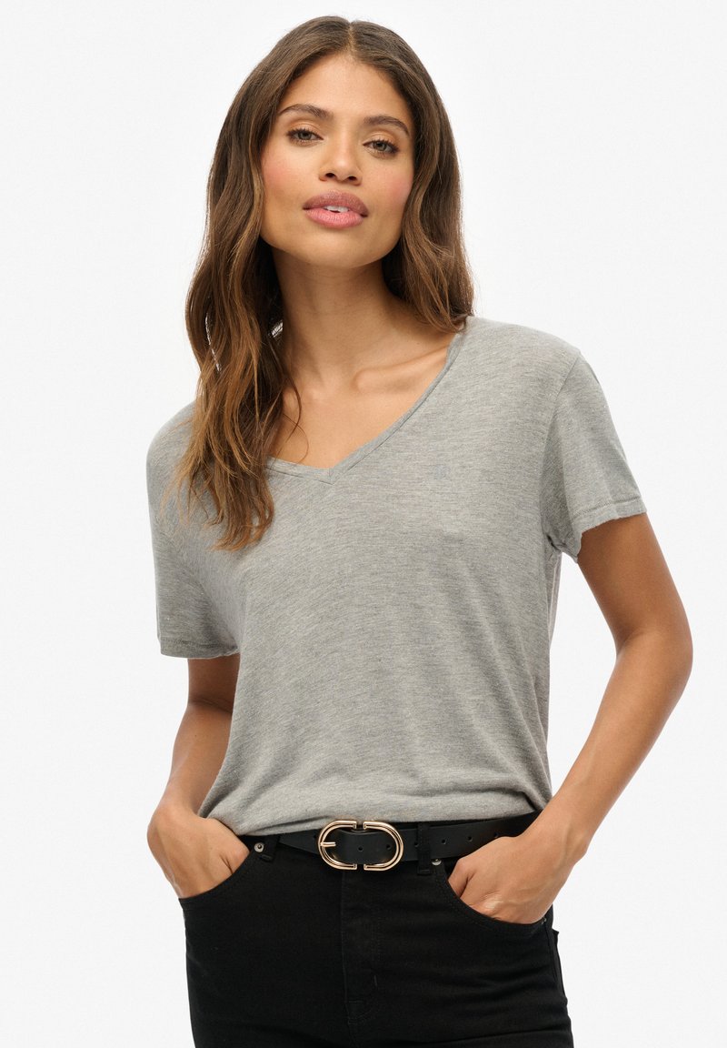 Camiseta gris de manga corta y escote en V, hecha de material suave, combinada con un cinturón negro con una hebilla de doble círculo dorada, usada con pantalones negros.
