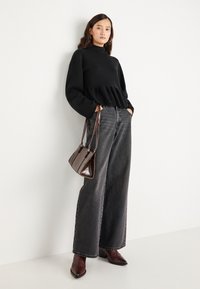 Svart strikket genser med peplumkant, sammen med grå denimjeans med vid ben. Tilbehør med en brun skinnveske og spisse ankelstøvler.