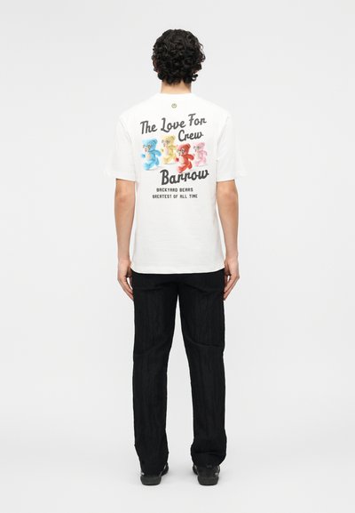 Άνδρας που φοράει λευκό μπλουζάκι με πολύχρωμες αρκουδίτσες και κείμενο «The Love For Crew Barrow Backyard Bears Greatest Of All Time» στην πλάτη.