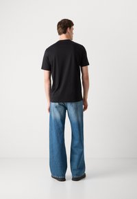 Zwarte T-shirt met korte mouwen, van katoen, met een standaard pasvorm, gecombineerd met lichtblauwe wijde jeans met vervagingseffect en zwarte schoenen.