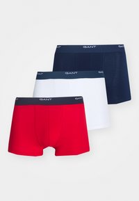 Trois paires de boxers pour hommes rouges, blancs et bleu marine, chacun avec une ceinture de marque indiquant "GANT".