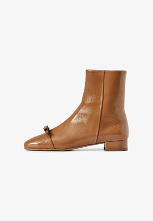 Stivaletti in pelle color tan con finitura lucida, punta a punta e un piccolo fiocco sulla parte anteriore. Tacco basso e spesso per maggiore stabilità.