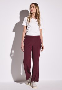Pantalons larges bordeaux avec une taille sans couture, associés à un t-shirt blanc à col rond et des baskets de teinte neutre.
