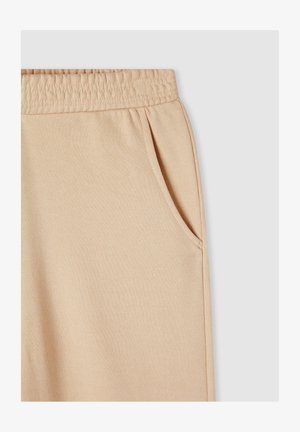 Beżowe dresy bawełniane z elastyczną talią, bocznymi kieszeniami i miękką fakturą. Gładki design bez widocznych wzorów.