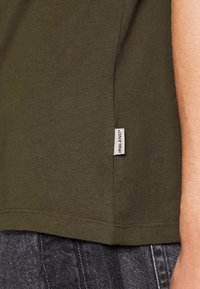 Olivengrøn T-shirt lavet af blødt stof, med et side søm etiket, i et enkelt design og standard pasform. Ingen synlige mønstre eller akcenter.