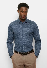Navy blue button-up shirt with a geometric pattern, long sleeves, and a spread collar, paired with light brown trousers and a black belt.