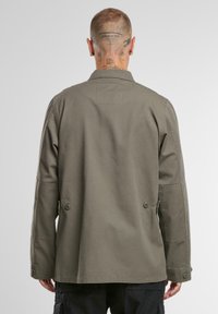 Chaqueta de algodón verde oliva con un corte relajado, que presenta un collar puntiagudo, dos botones en la parte de atrás y bolsillos en las costuras laterales.