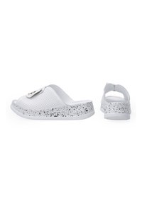 Witte instapsandalen met geperforeerde bovenkant, gespikkelde zwart-witte zool en een klein embleemdetail. Open achterkant voor gemakkelijke aan- en uittrekken.