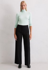 Langärmliges Turtleneck-Shirt in hellem Mintgrün, kombiniert mit hochtaillierten, weiten schwarzen Hosen. Glattes Material mit minimalen Nähten.