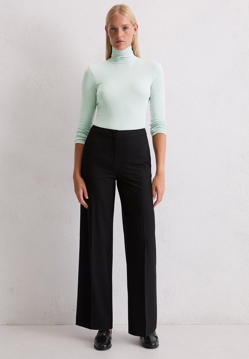 Langärmliges Turtleneck-Shirt in hellem Mintgrün, kombiniert mit hochtaillierten, weiten schwarzen Hosen. Glattes Material mit minimalen Nähten.