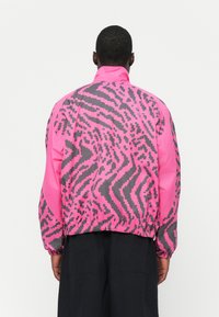 Pink and gray jacket with a geometric pattern, featuring an elastic waistband and high collar. Made from a lightweight material.