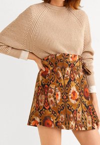 Beige neulepaita, jossa on löysät hihat, yhdistettynä ruskeaan ja oranssiin kuviolliseen mini-hameseen, jossa on kukkasuunnitelmia ja solmittava vyötärö.