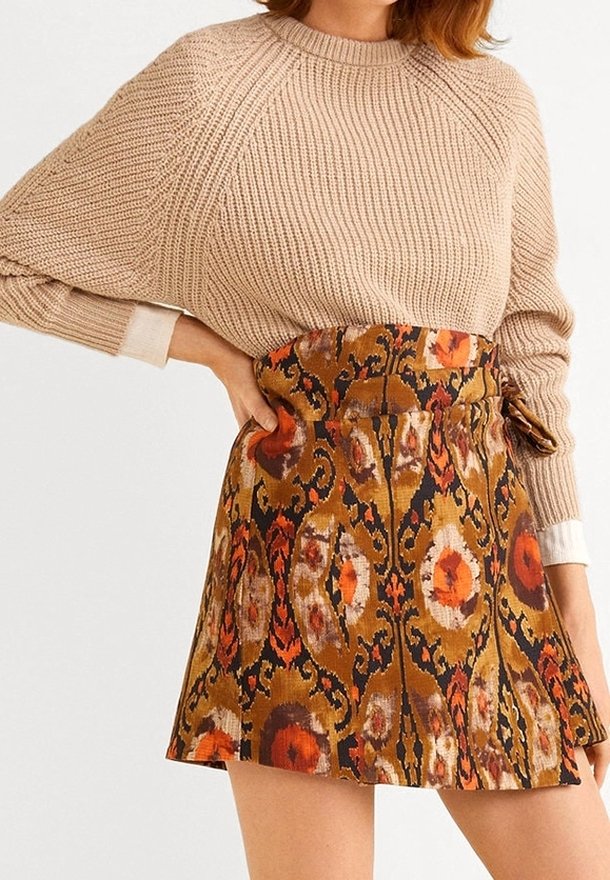 Beige neulepaita, jossa on löysät hihat, yhdistettynä ruskeaan ja oranssiin kuviolliseen mini-hameseen, jossa on kukkasuunnitelmia ja solmittava vyötärö.