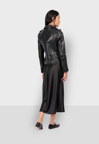 Černá kožená motorkářská bunda se zipovými manžetami, přiléhavým střihem a detailními švy na ramenou, nošená přes hladké černé midi šaty.